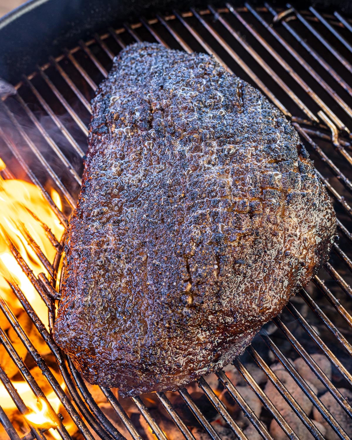 Whole picanha searing over live charcoal flame, fat cap rendering and bubbling