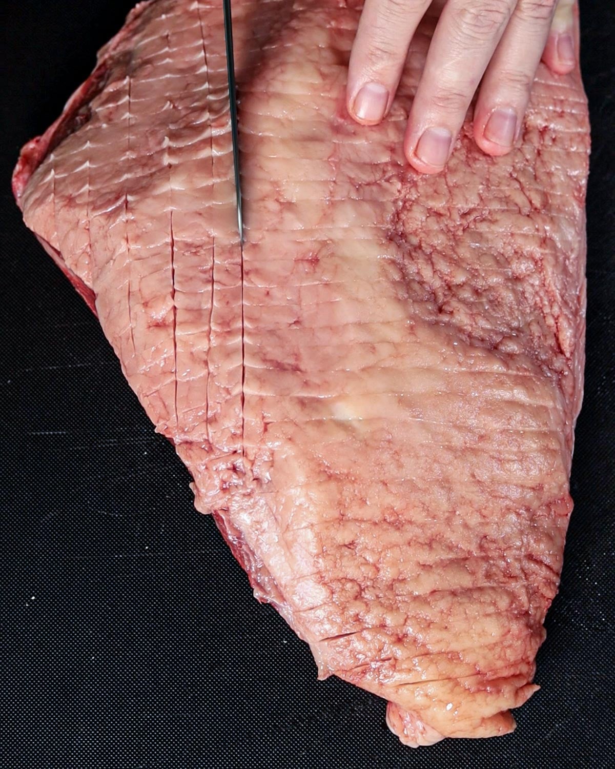 Scoring the fat cap of a whole picanha roast in a crosshatch pattern before seasoning