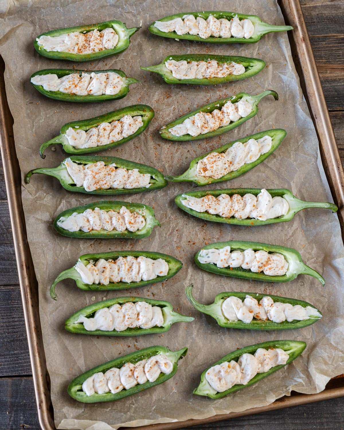 Jalapeño halves filled with seasoned cream cheese mixture on a parchment-lined sheet tray before wrapping