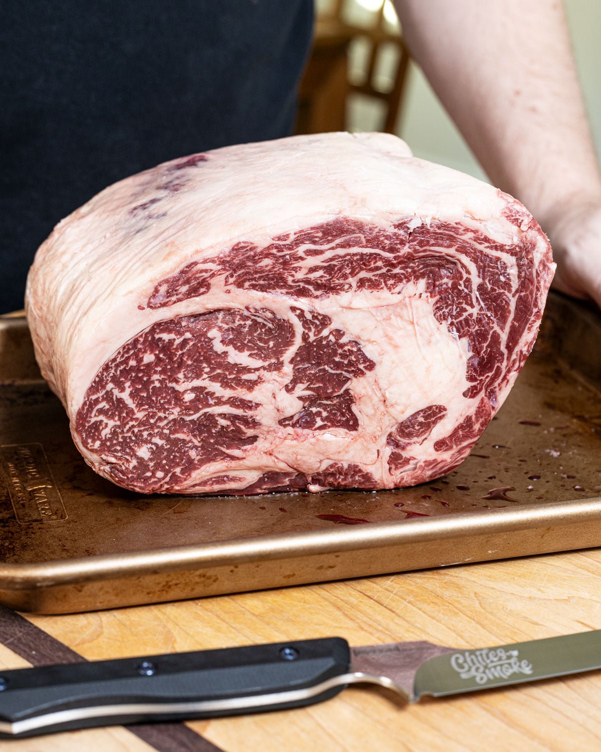 raw prime rib roast with visible marbling, resting on a sheet pan before trimming