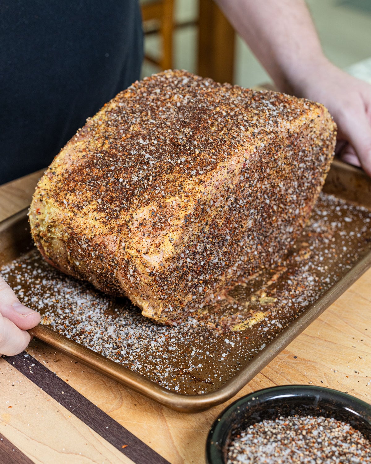 seasoned prime rib roast coated in dry rub, being placed on a sheet pan