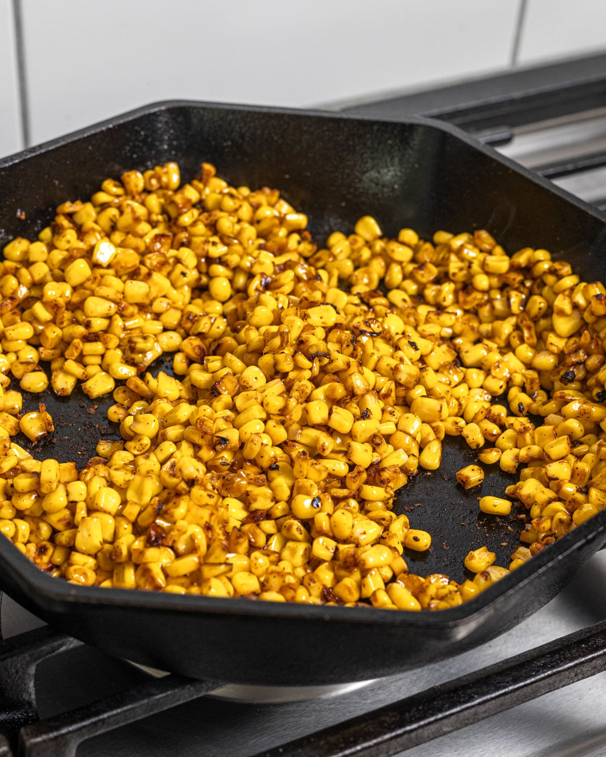 Corn is starting to char in a cast iron skillet on the stove.