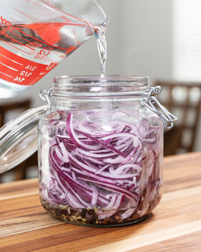 Pour the lukewarm pickle brine over the sliced red onions and aromatics.