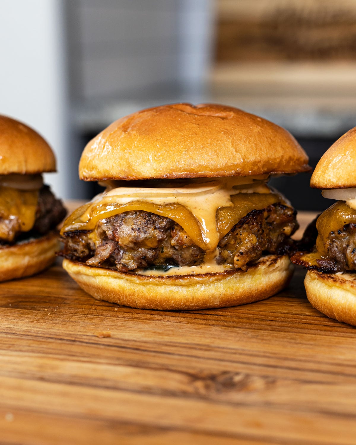 Three crack burgers with melted cheddar, BBQ ranch sauce, and raw onion on toasted brioche buns