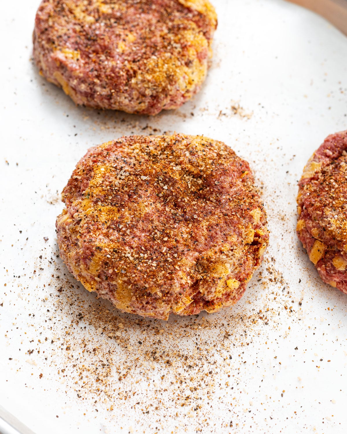 Formed crack burger patties seasoned with Canyon Crust beef seasoning on a sheet pan, ready for the griddle