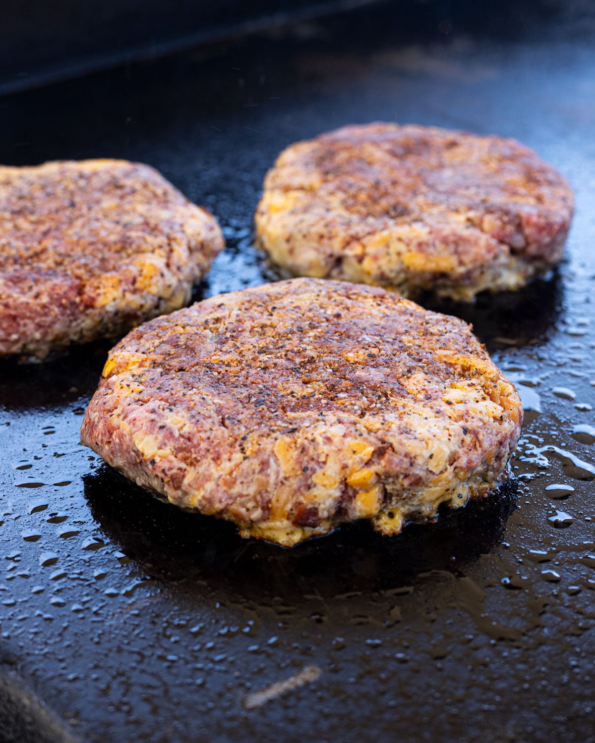 Raw crack burger patties with shredded cheddar visible, seasoned with Canyon Crust and placed on a hot griddle