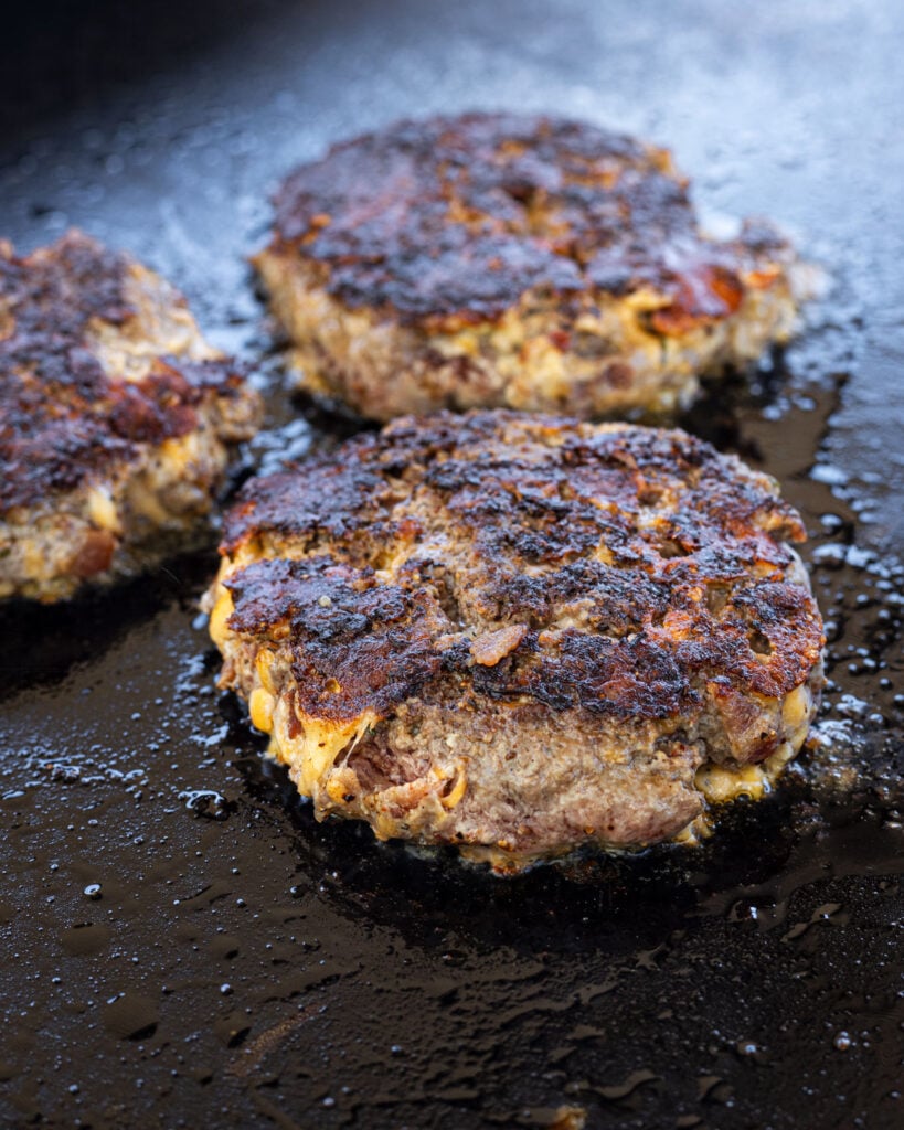 Flip the crack burger patties and build a crust on the second side. The cheese is melting and forming a crispy cheese skirt.