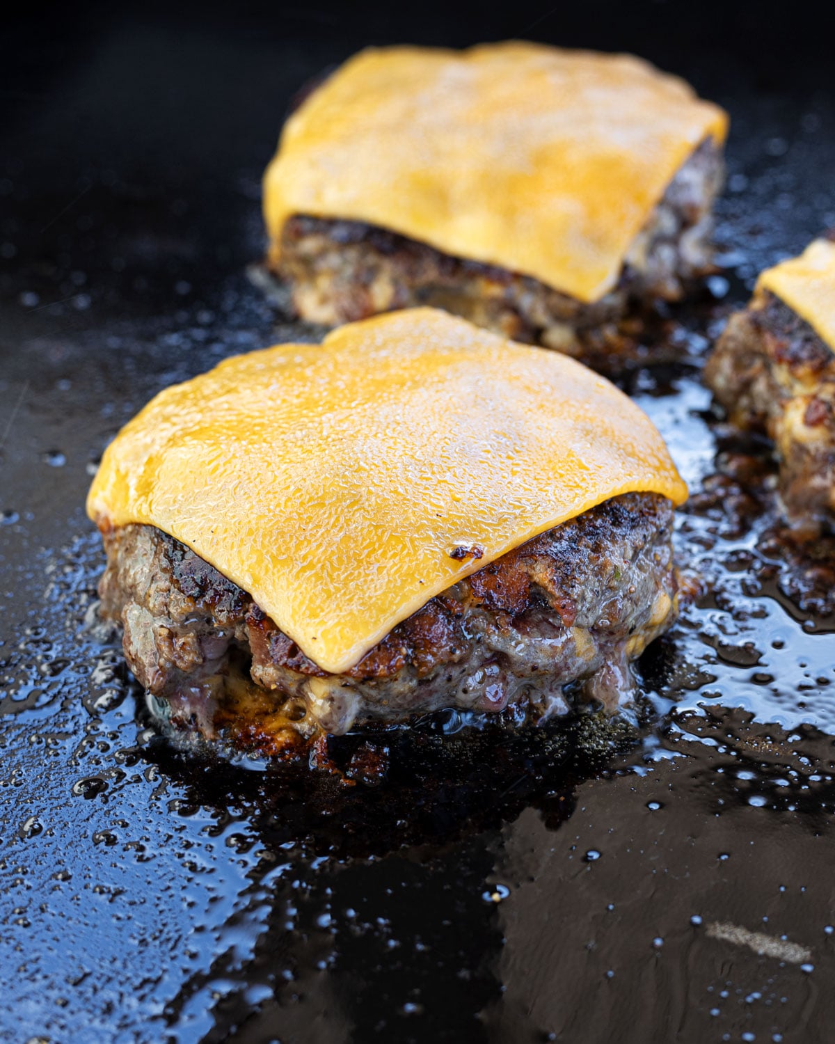 Crack burger patties topped with melted American cheese slices on a flat-top griddle