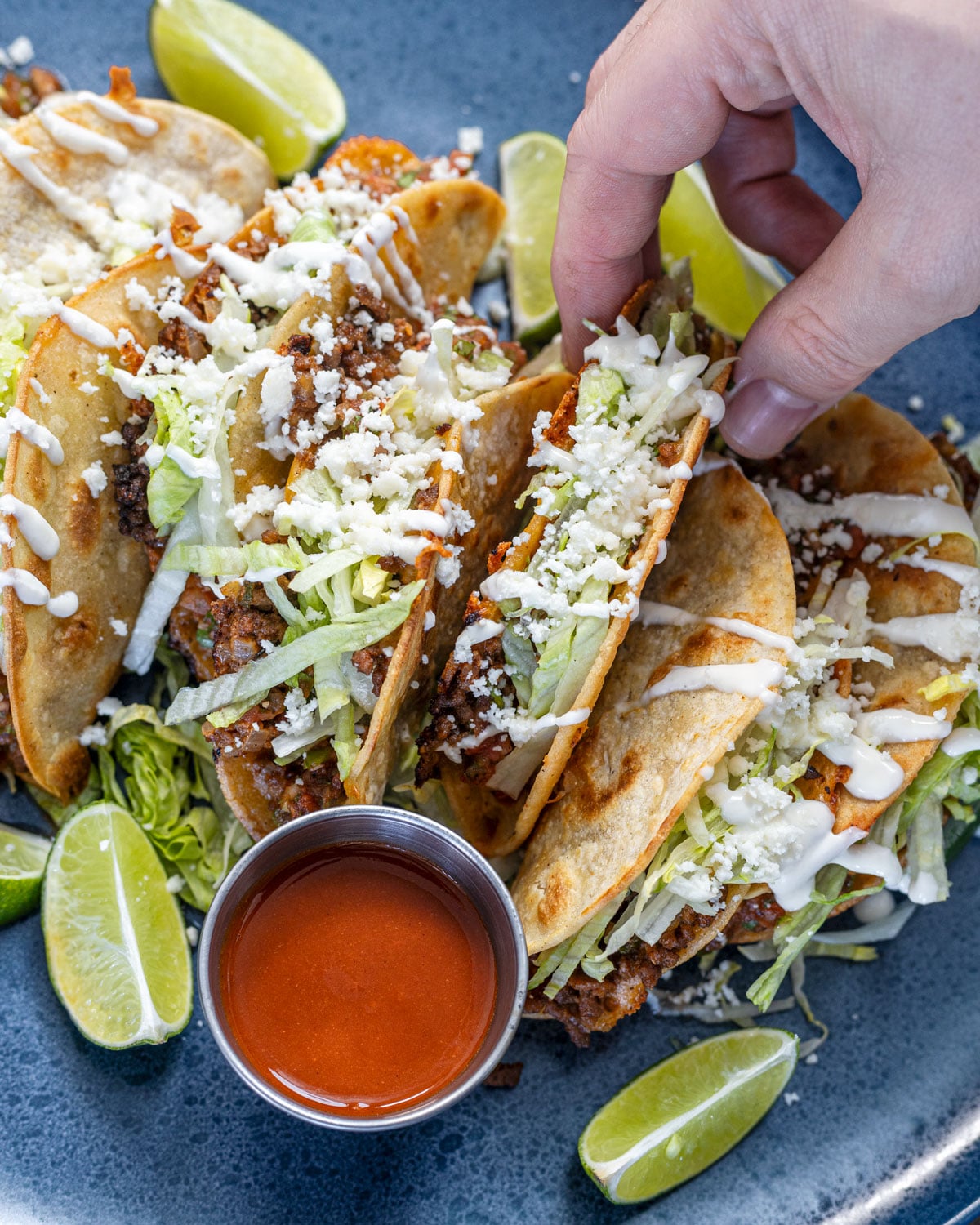 Overhead view of tacos dorados on a blue plate with red salsa, lime wedges, and jalapeño