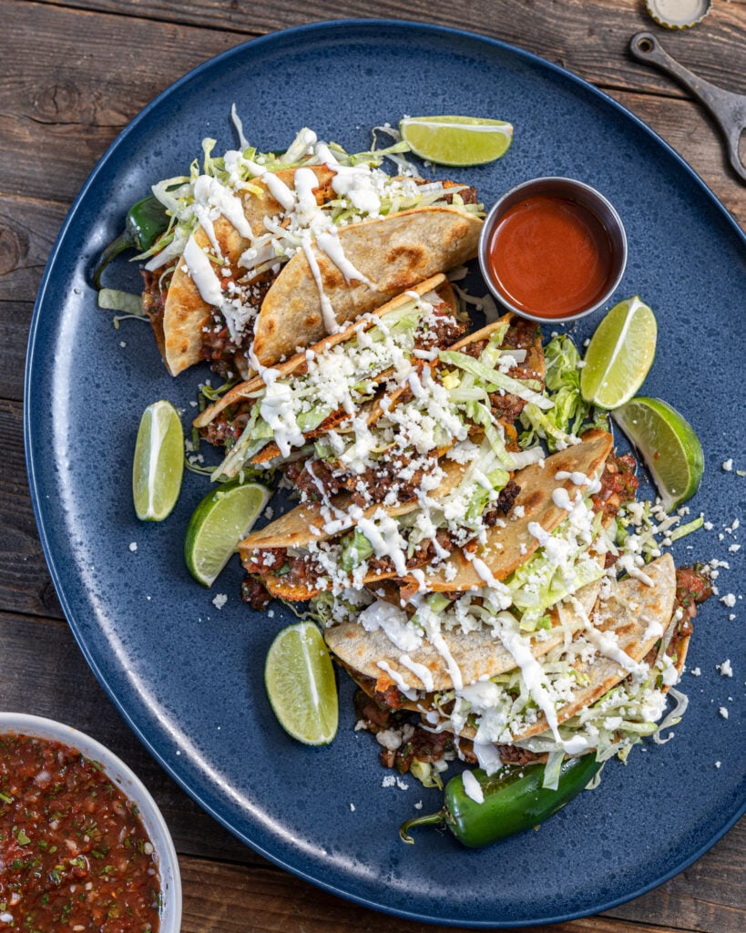 Serve a plate of crispy tacos dorados with plenty of toppings.