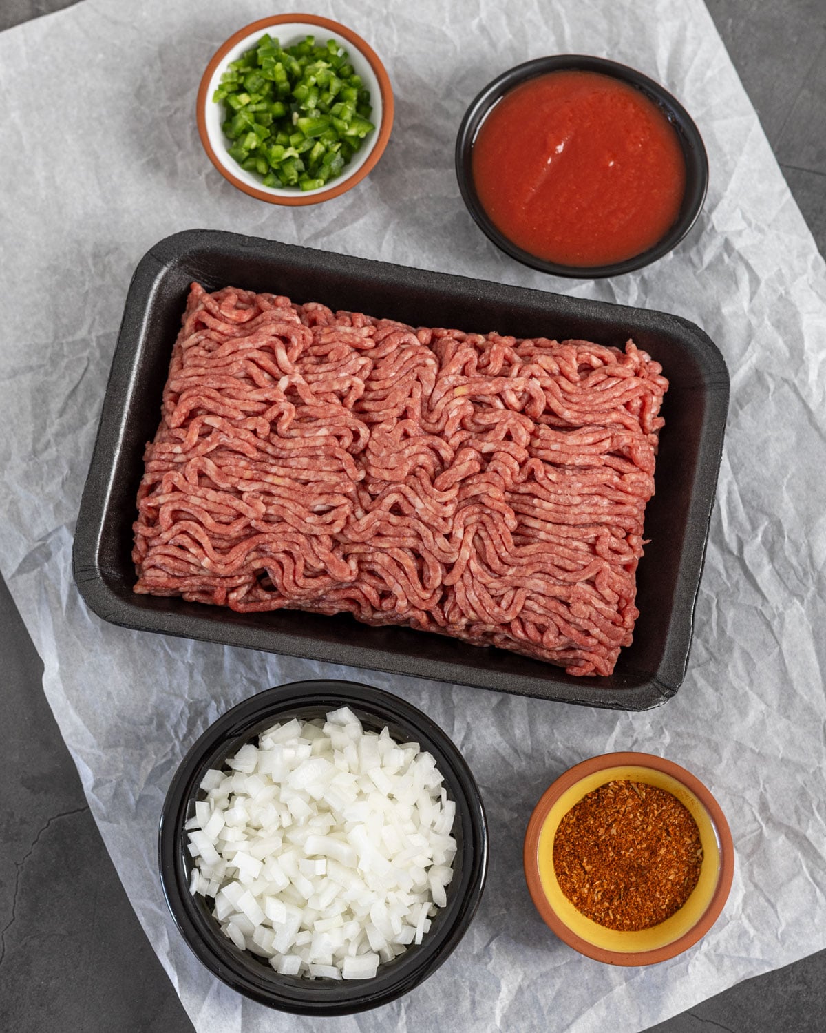 Raw ground beef with diced white onion, jalapeño, tomato sauce, and taco seasoning in prep bowls