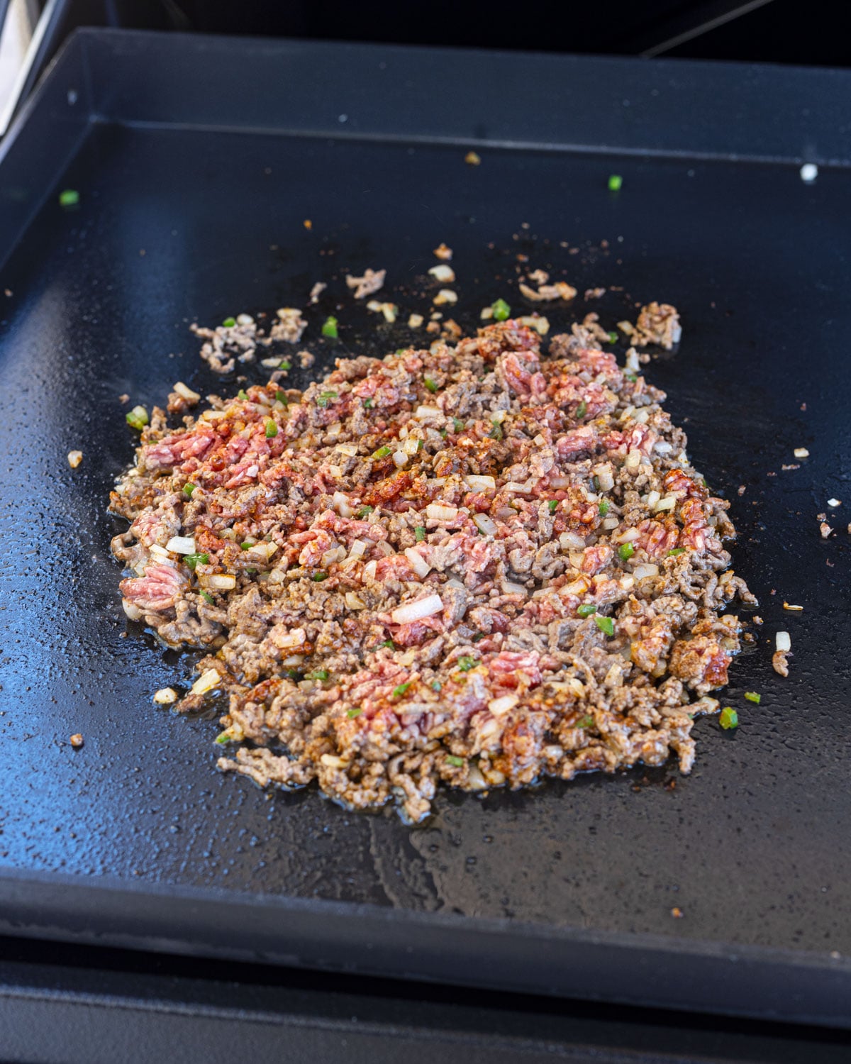 Seasoned ground beef with onion and jalapeño cooking on a griddle