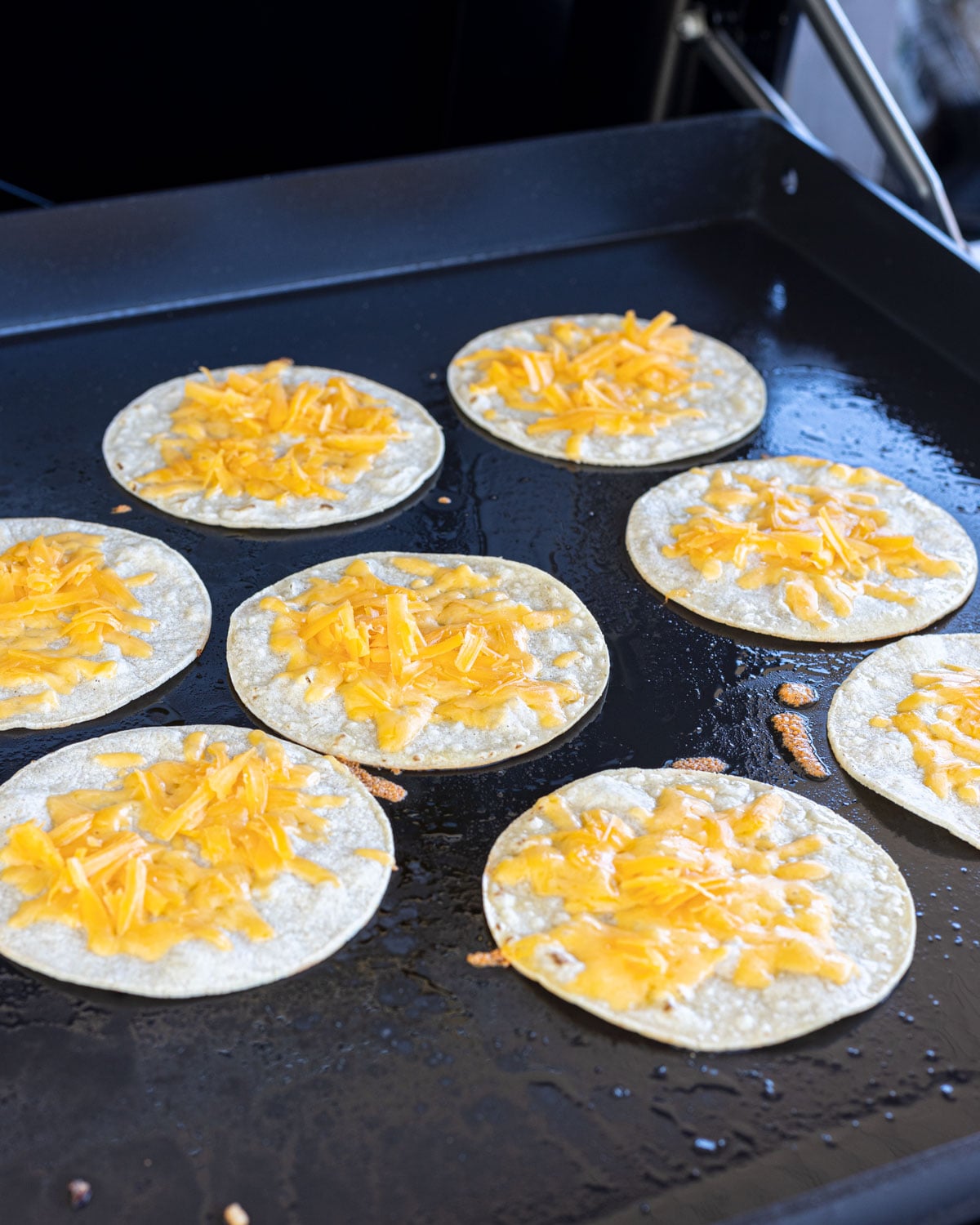 Corn tortillas topped with shredded cheddar melting on a griddle