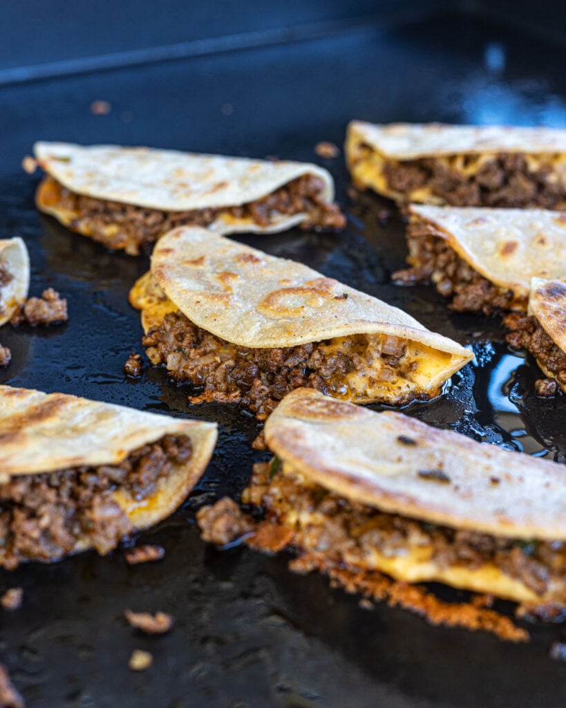 These crispy tacos dorados are frying up on a hot griddle, loaded with cheese.