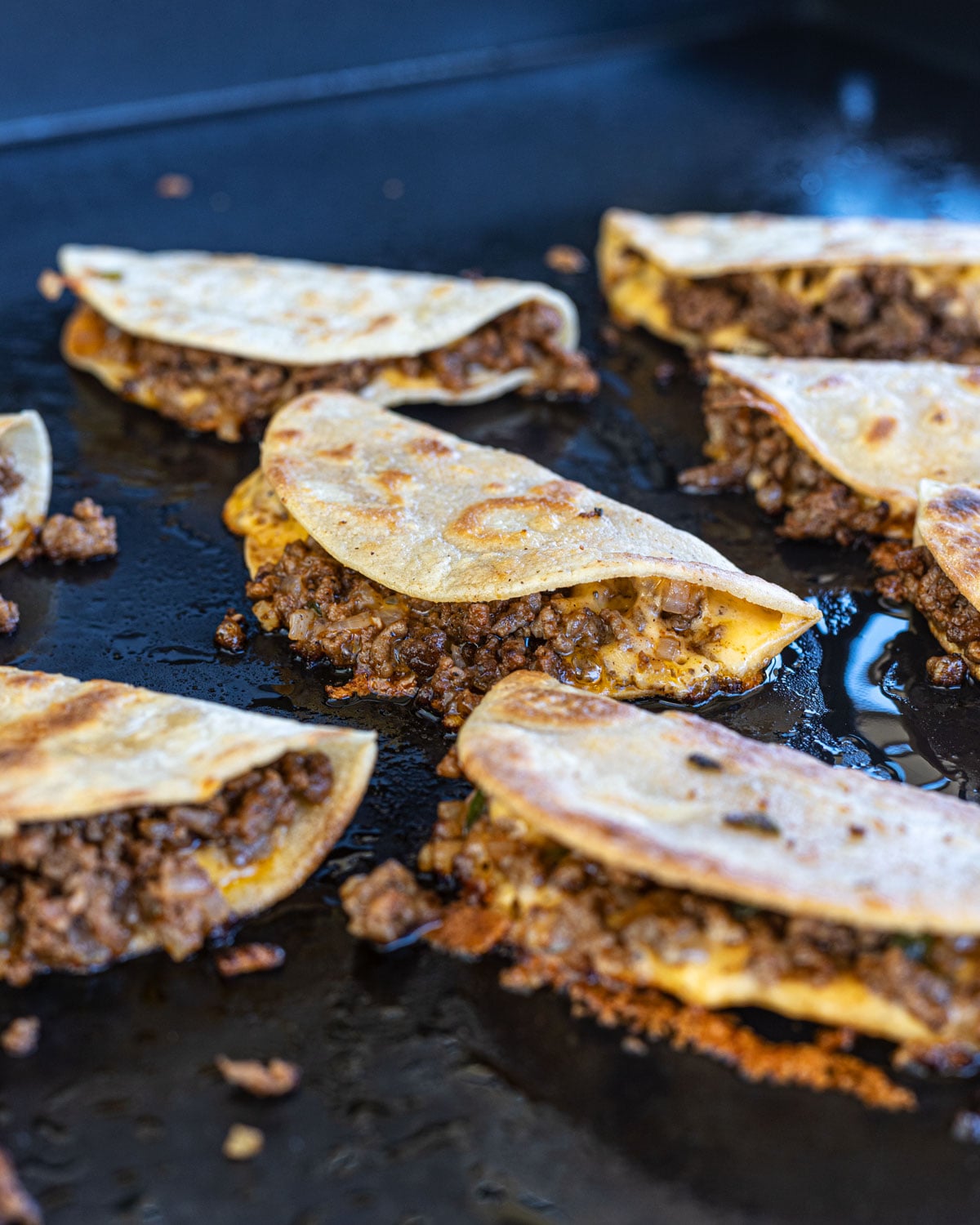 Golden-brown tacos dorados frying on a griddle showing crispy shells