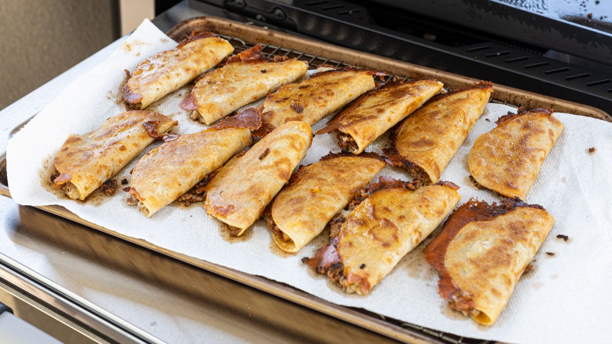 Fried tacos dorados draining on a paper-towel-lined tray