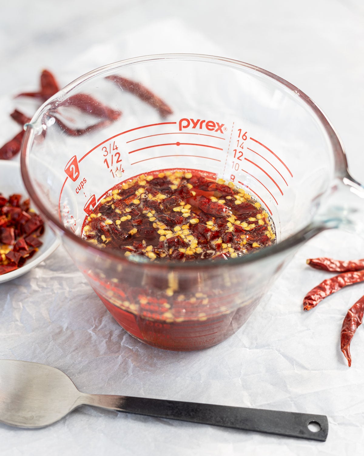 Chiles de arbol hot honey resting in a Pyrex measuring cup after warming, with apple cider vinegar stirred in
