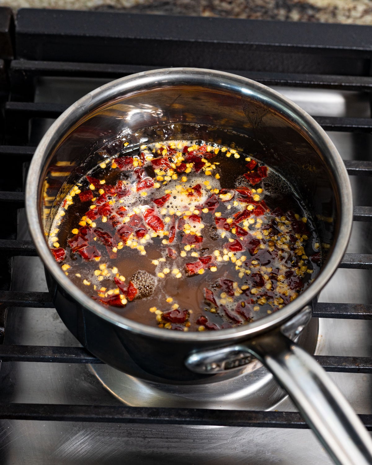 Chiles de arbol and honey simmering in a small saucepan on the stovetop