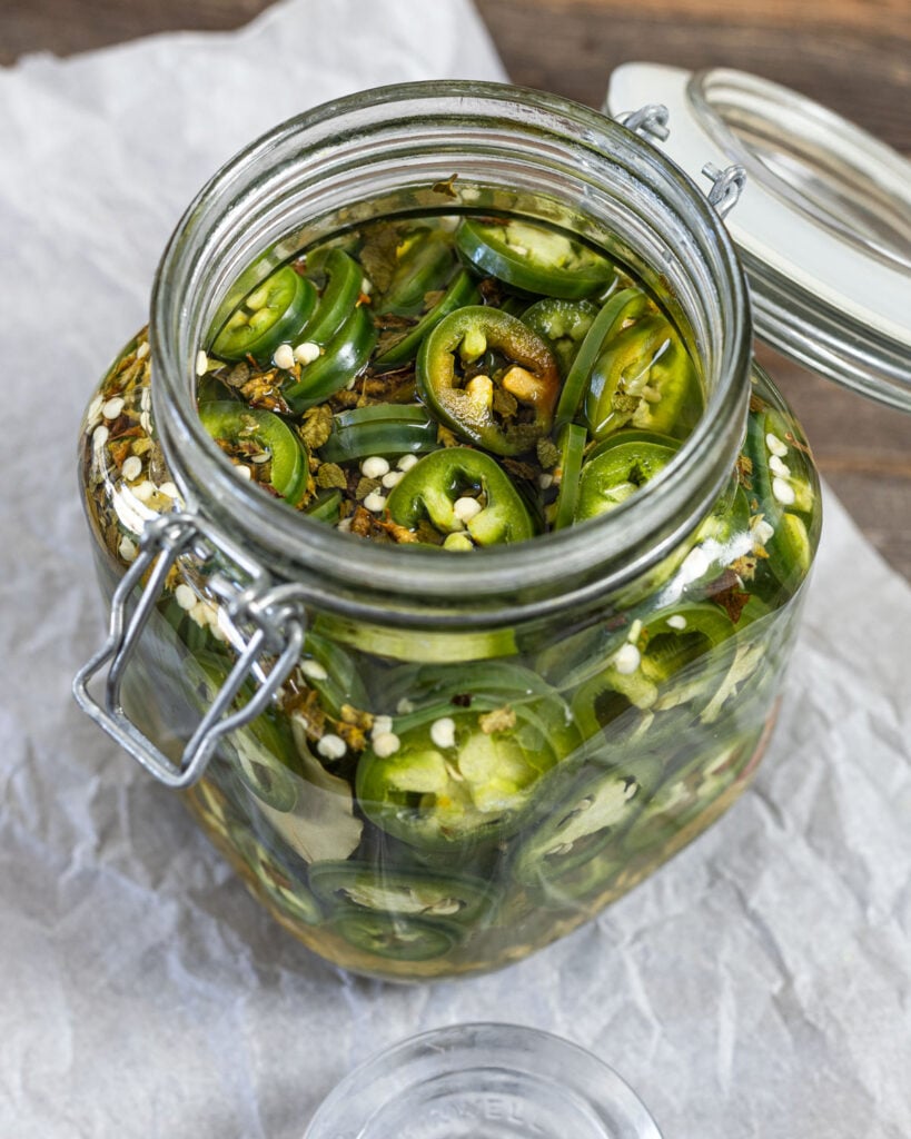 Pour the warm brine over the jalapenos and ingredients in the glass jar.