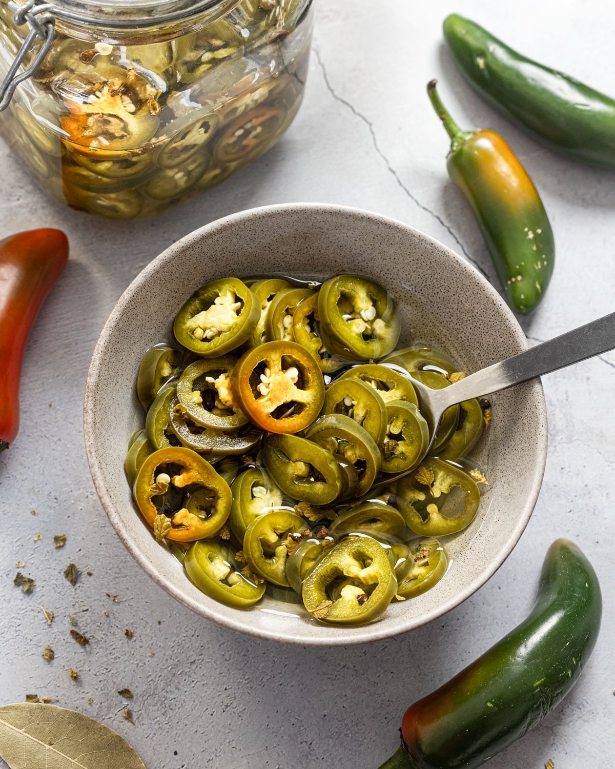 Quick pickled jalapeño rings served in a ceramic bowl with a spoon, glass jar and fresh jalapeños in the background