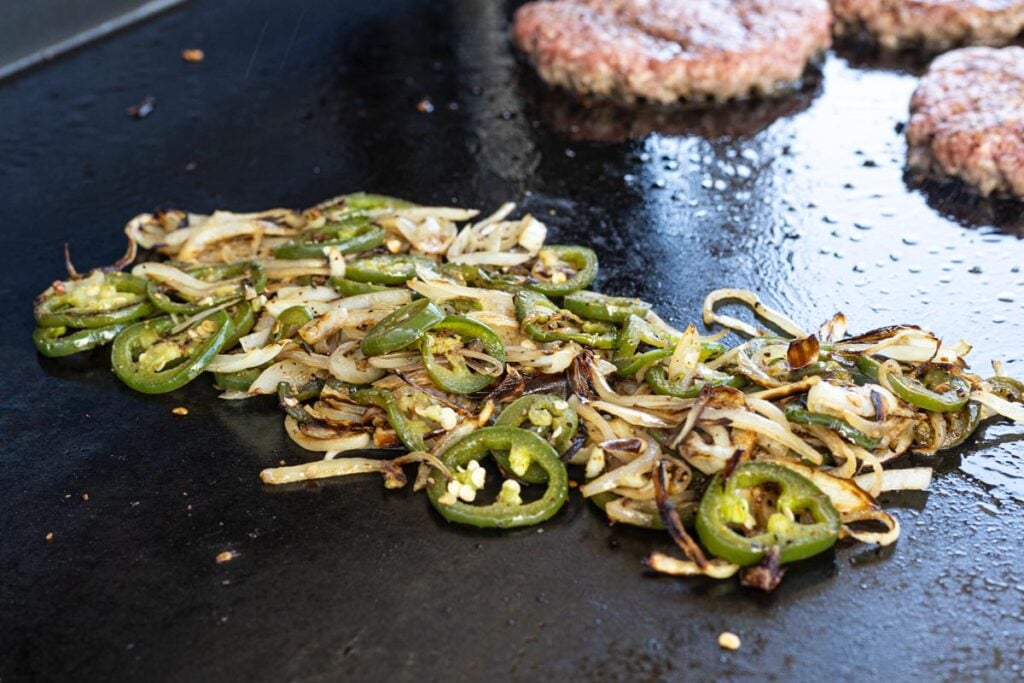 Jalapenos and onions are cooking slowly on the griddle alongside the burgers.