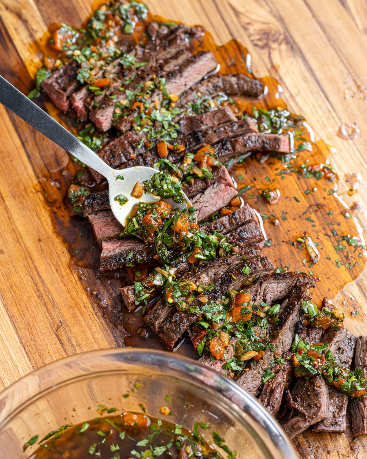 Sliced grilled steak topped with red chimichurri, a spoon draping the sauce over the slices