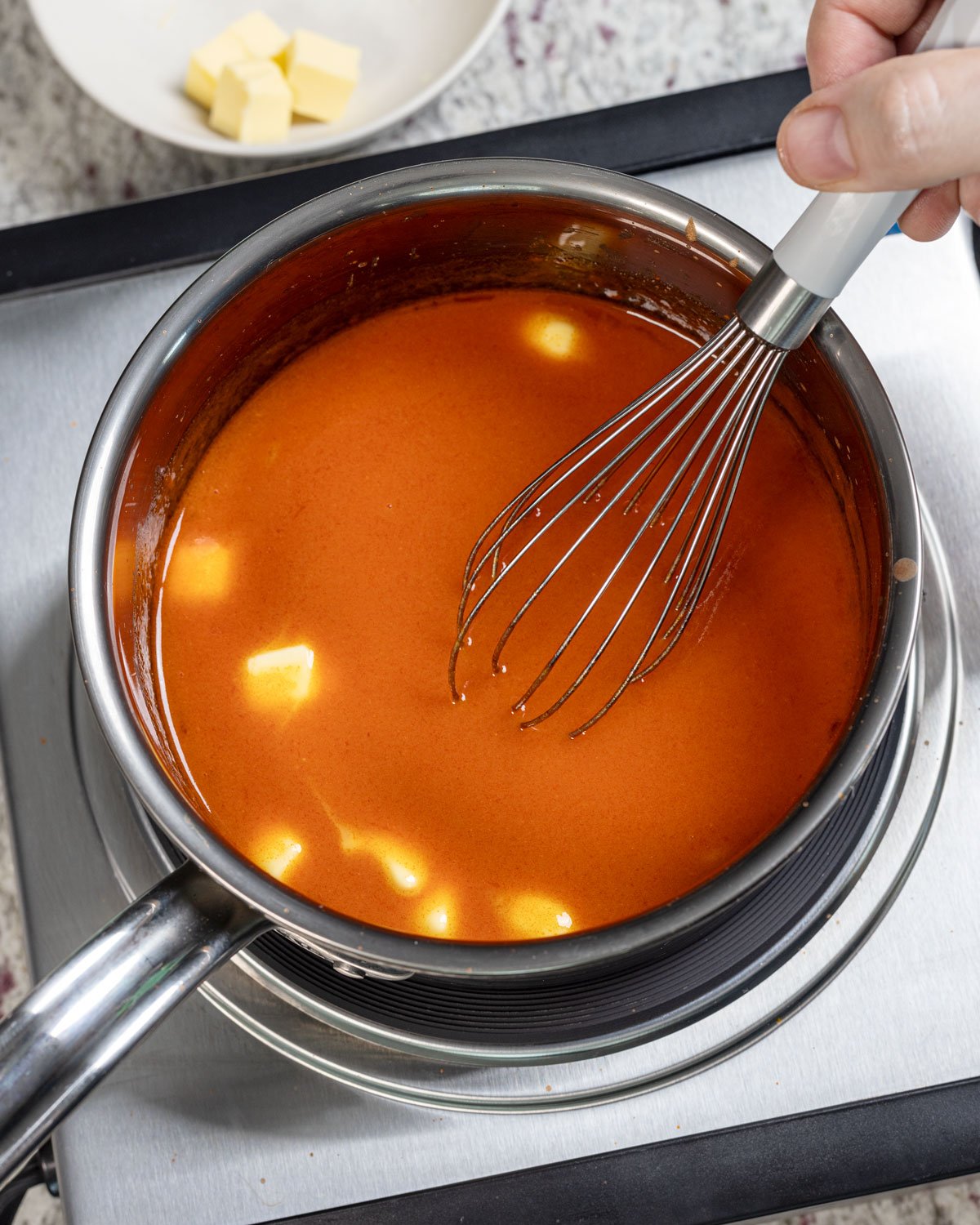 Whisking the butter into the warm hot sauce in a pan.