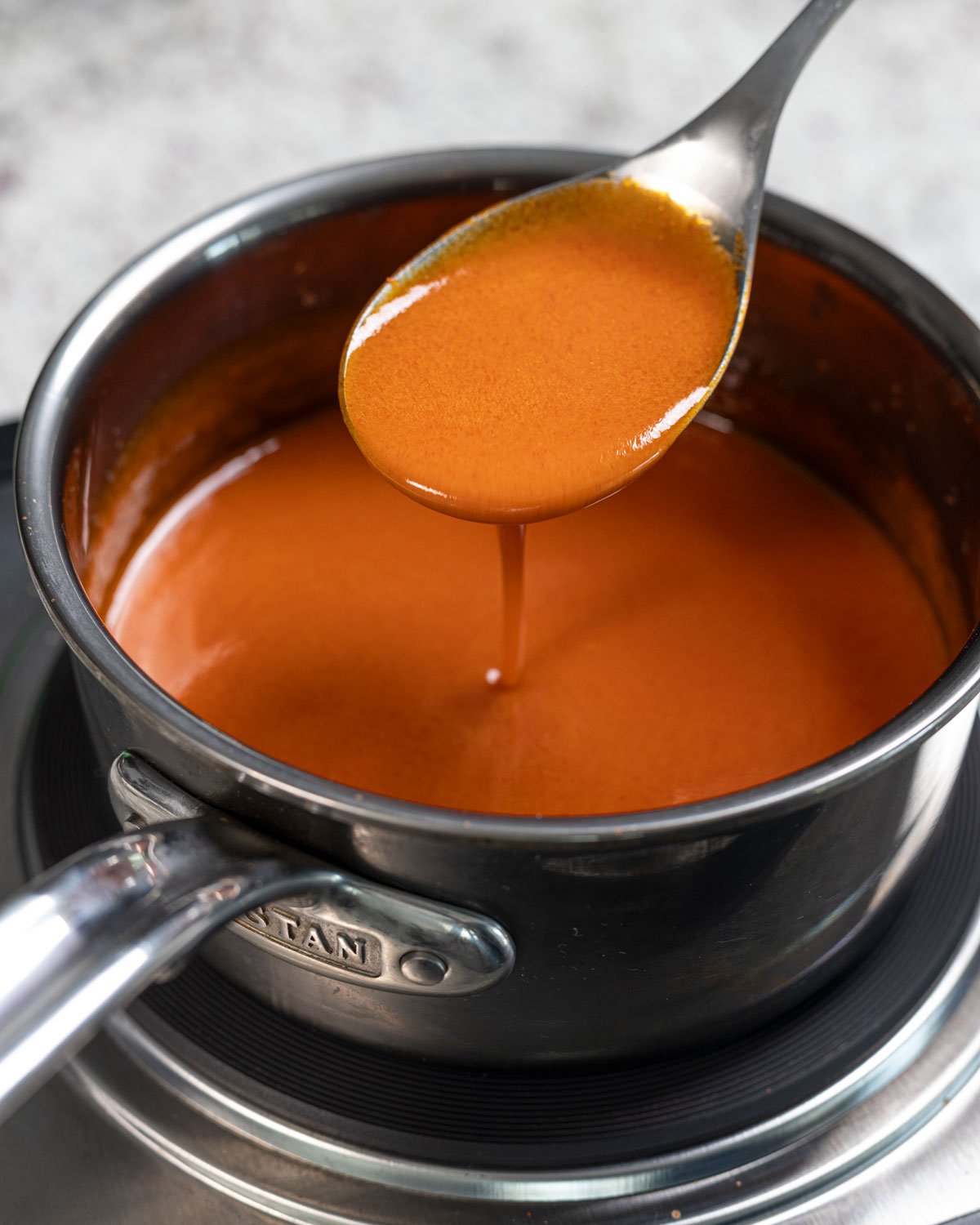 Homemade buffalo sauce dripping in a pan with a spoon