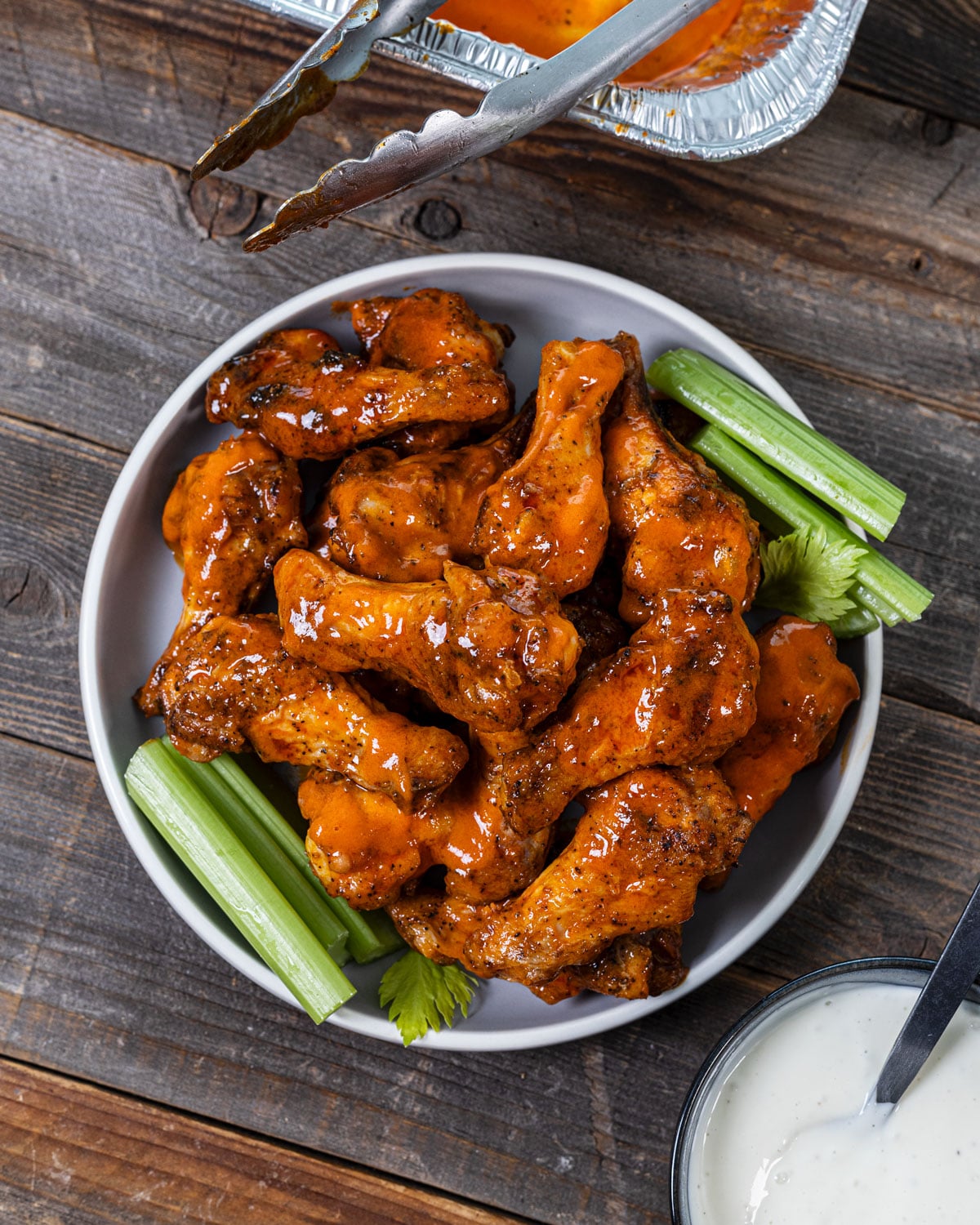 Buffalo wings tossed in sauce on a plate with celery sticks and ranch