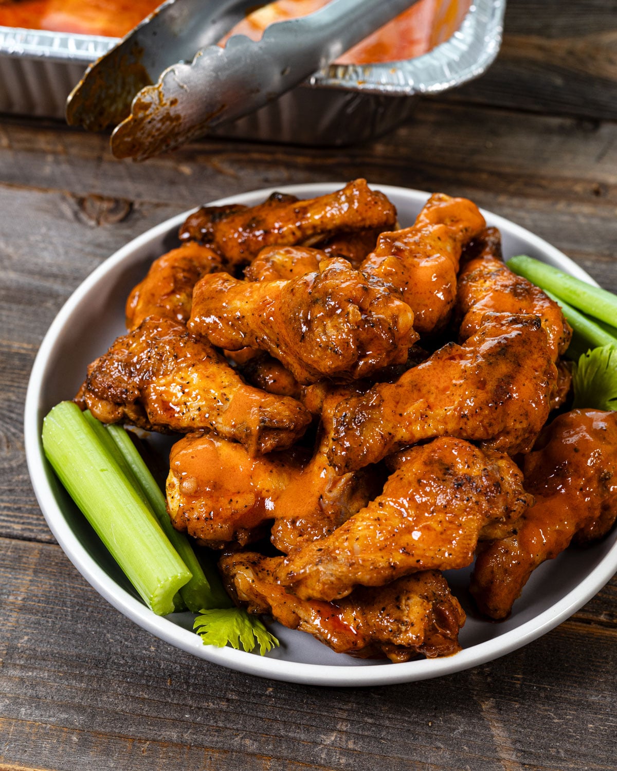 Buffalo wings tossed in sauce, plated with celery sticks
