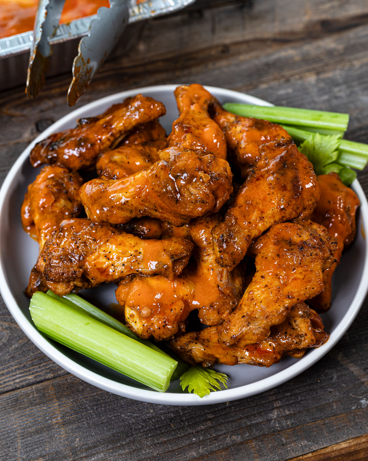 Homemade buffalo wings on a plate with celery next to grilling tongs