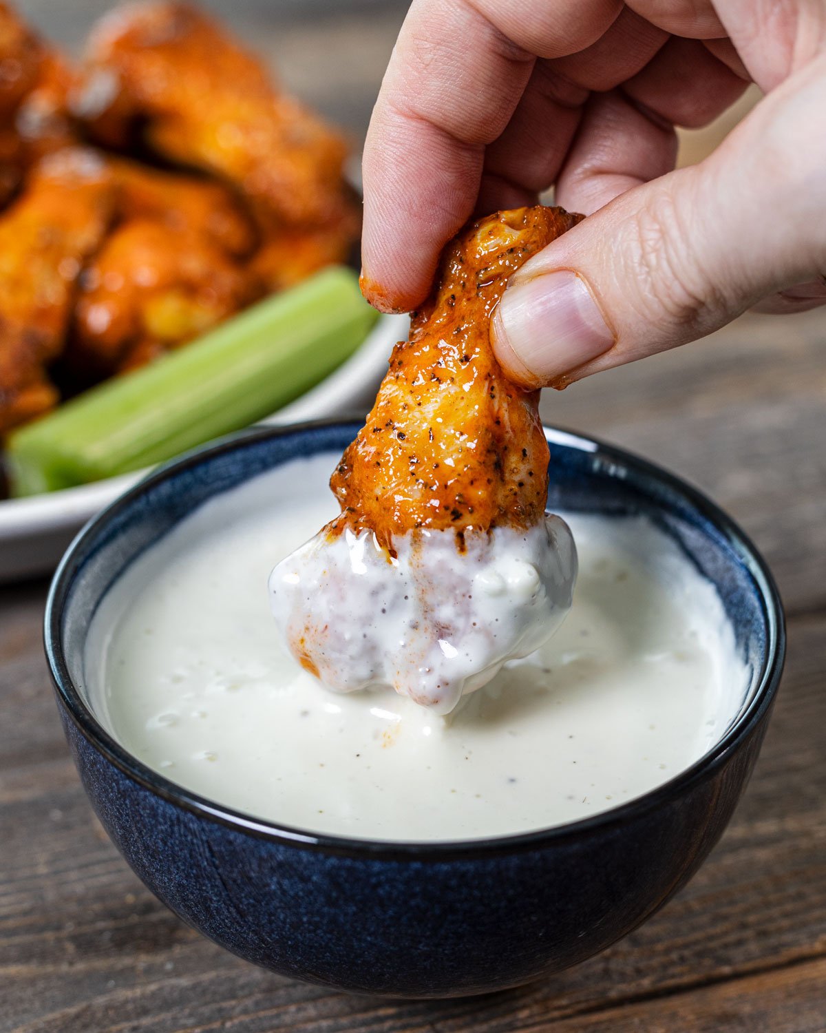 Hand dipping a grilled buffalo wing into a small bowl of blue cheese dressing.