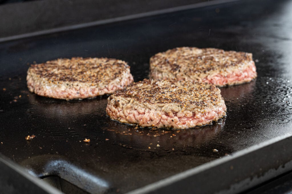 Burgers are searing on the griddle.