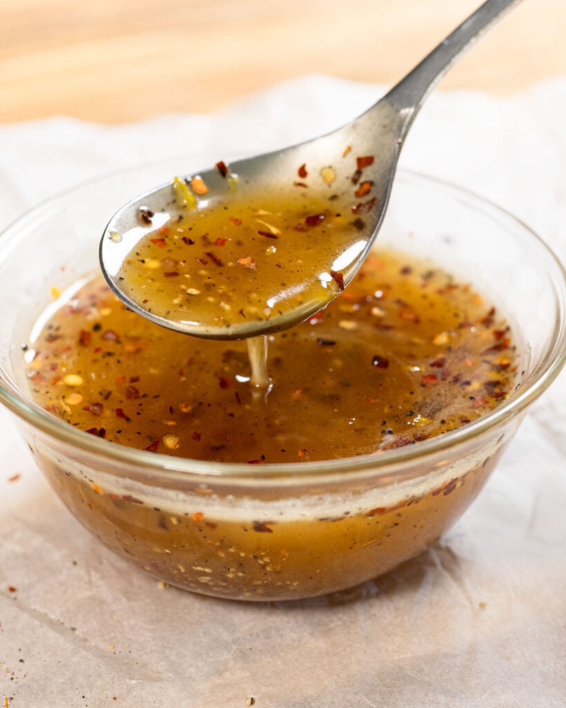 Hot honey lemon pepper wing sauce in a white bowl with a spoon scooping some sauce.