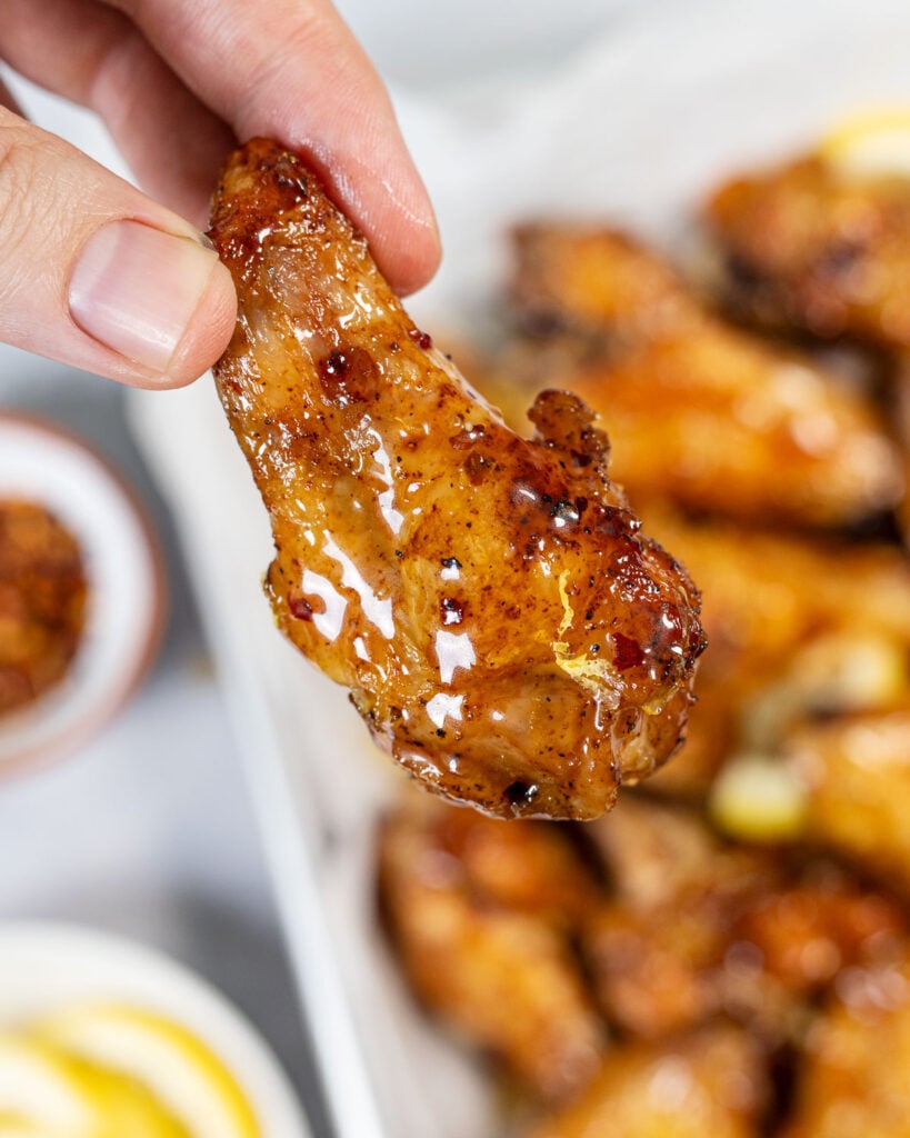 Hand holding a hot honey lemon pepper wing with more wings in the background.