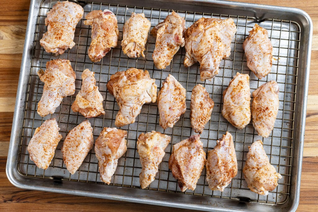 Raw chicken wings seasoned and placed on a baking sheet lined with a wire rack.