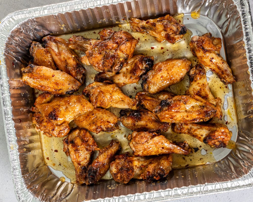 Wings being coated in the lemon pepper sauce in a foil pan.