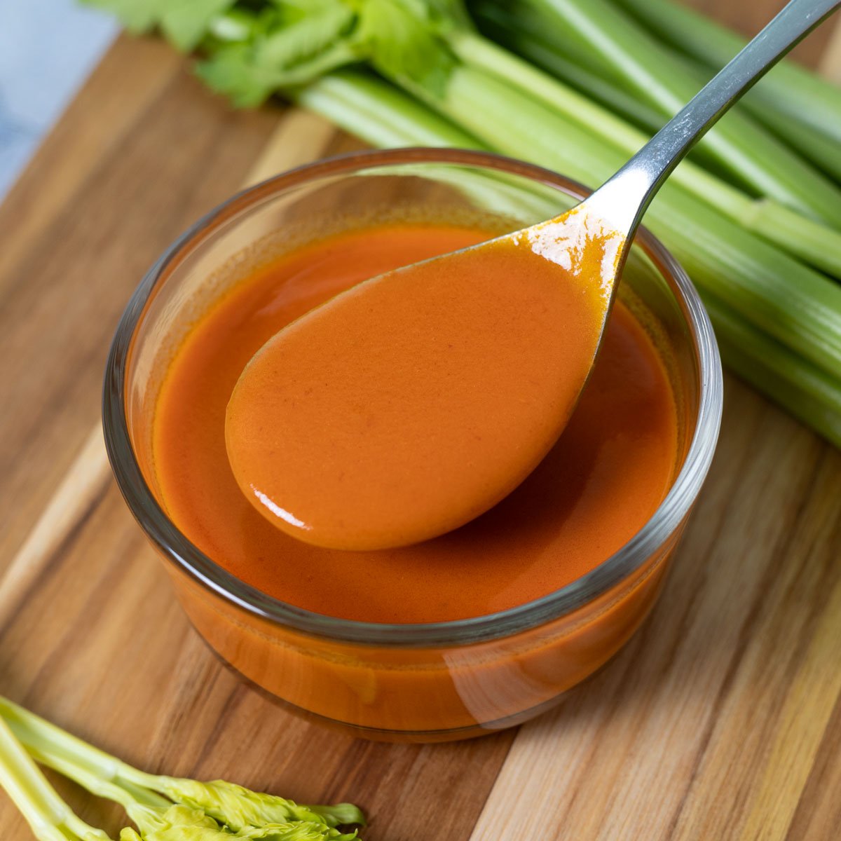 Homemade buffalo sauce is creamy, sitting on a spoon over a glass bowl