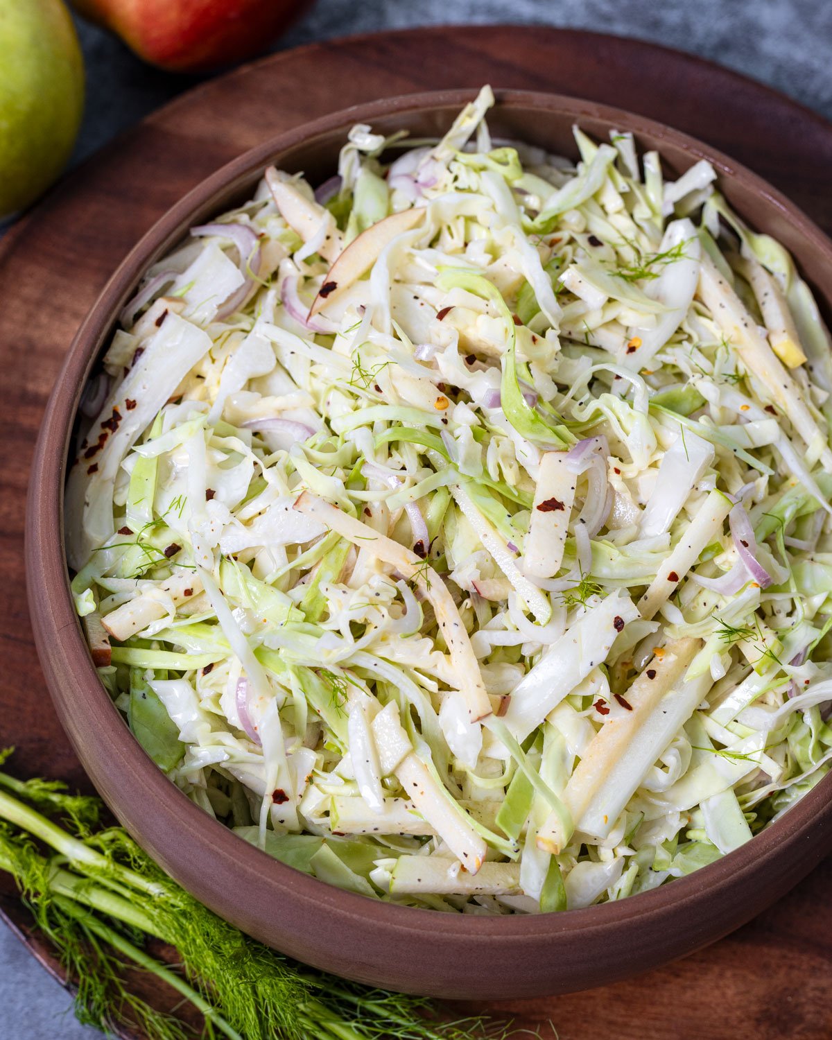 Apple and fennel coleslaw salad in a large serving bowl on a wooden background.