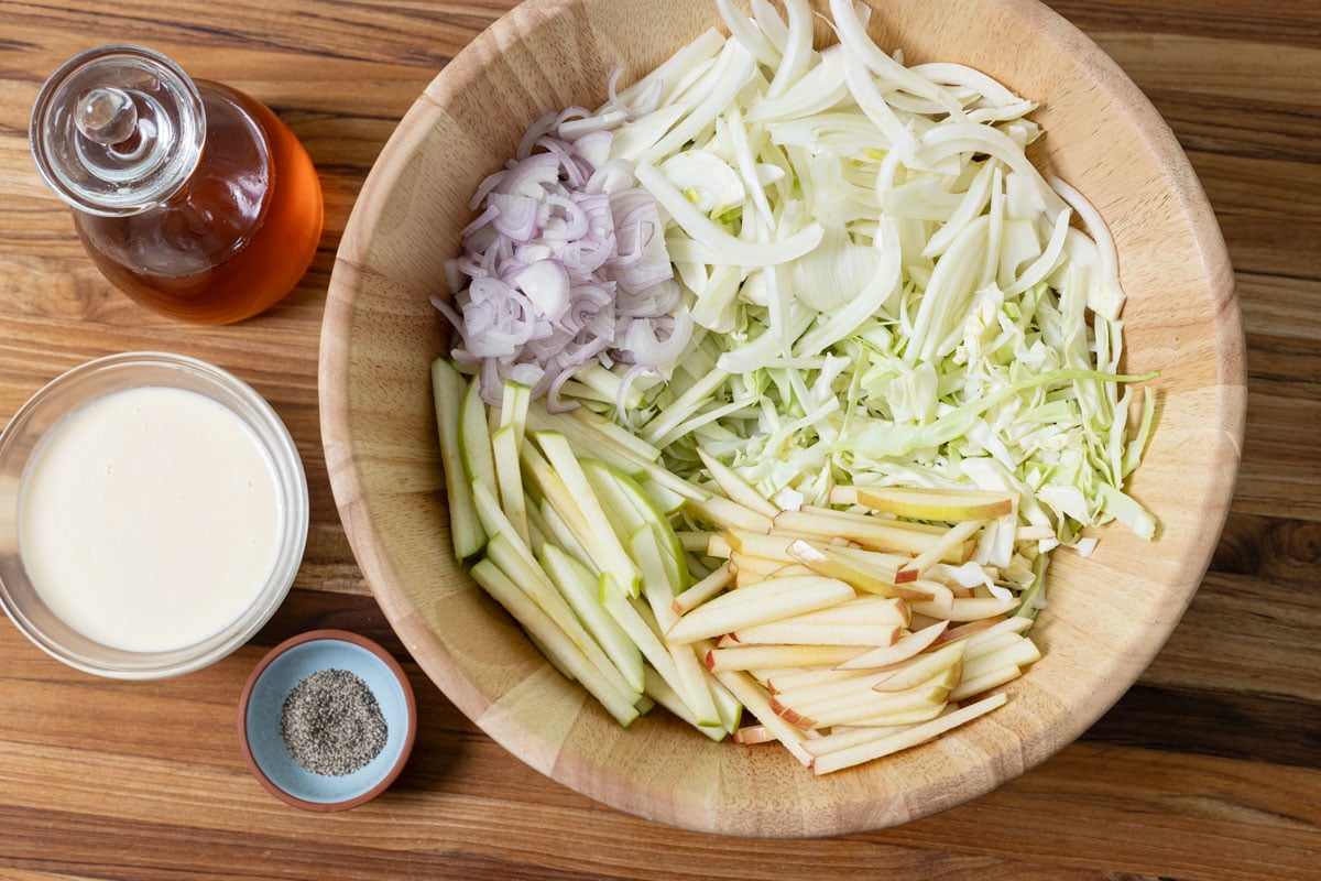 Prepped vegetables in a salad bowl with the dressing ingredients on the side.