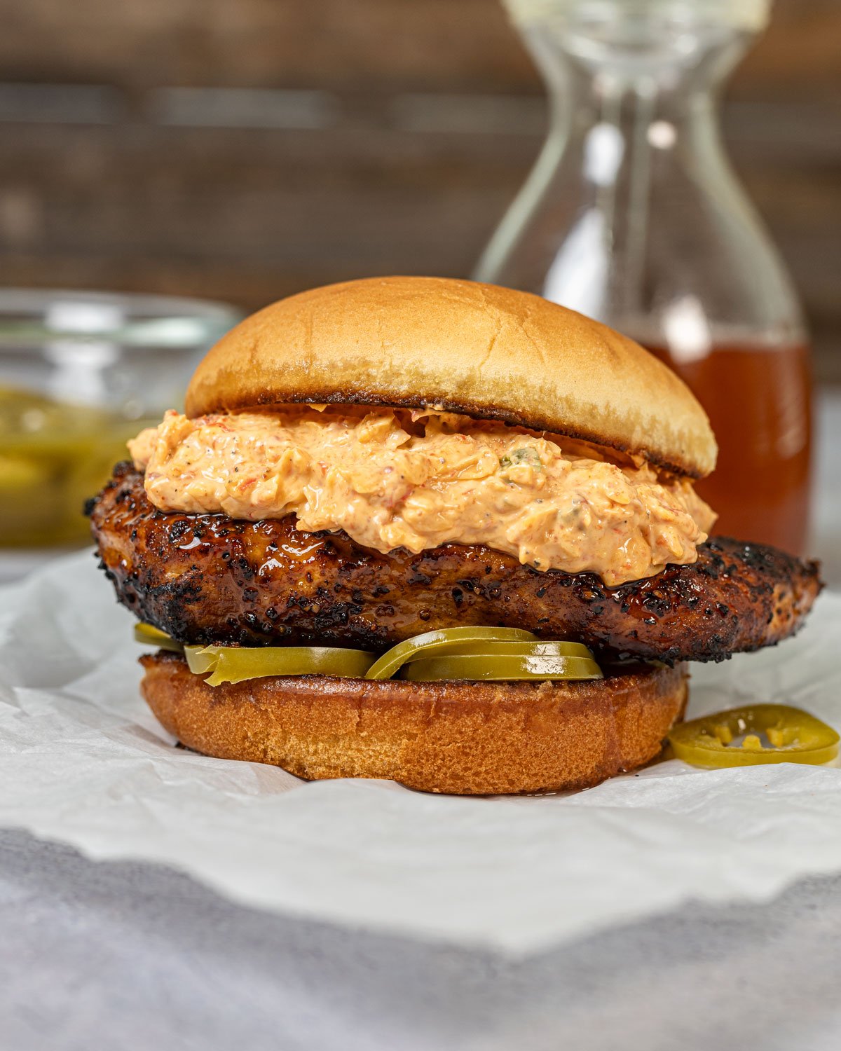 Side view of a grilled chicken sandwich with layers of pickled peppers and pimento cheese on a bun.