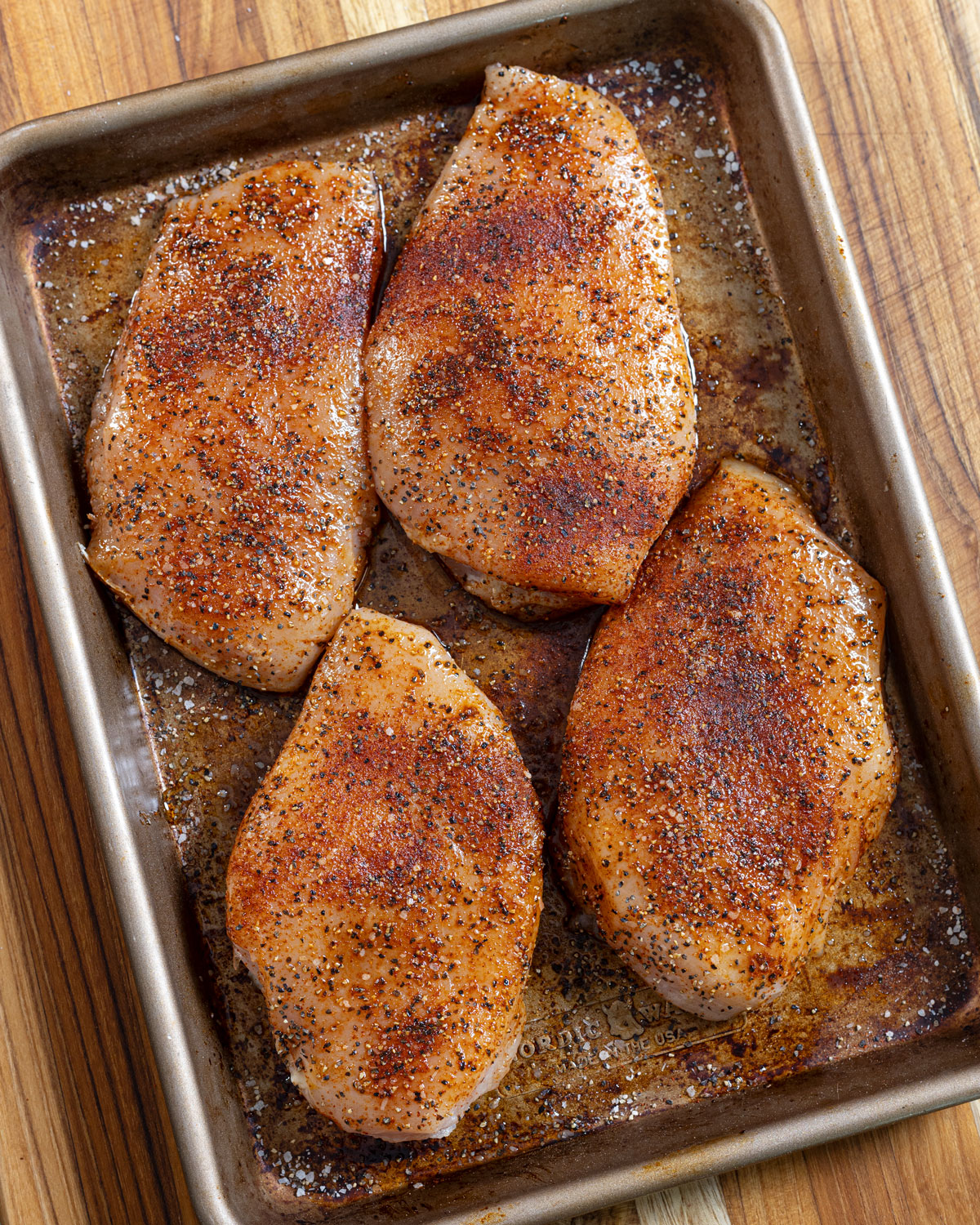 Four seasoned chicken breasts in a baking sheet.