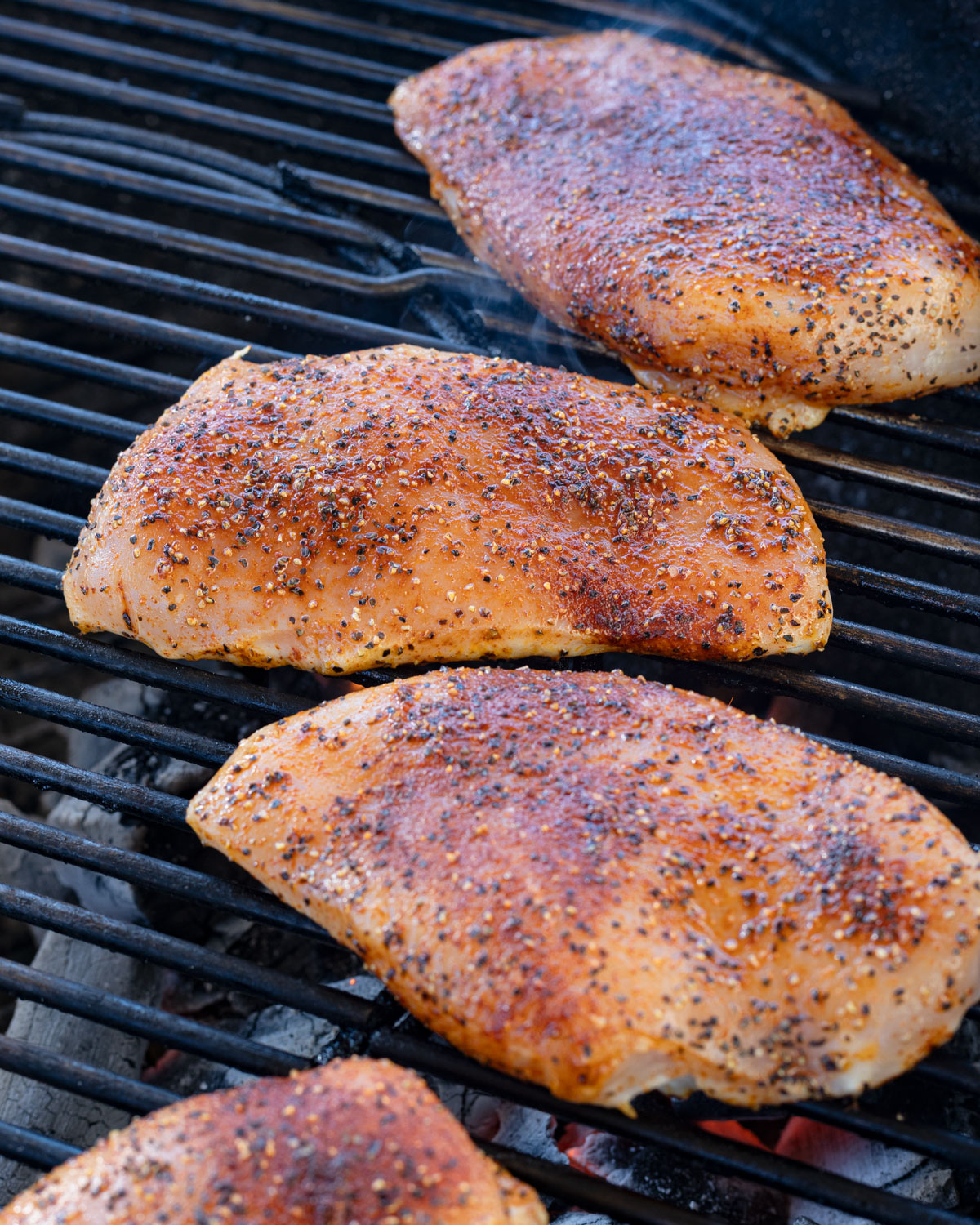 Seasoned chicken breasts starting to cook on a grill.