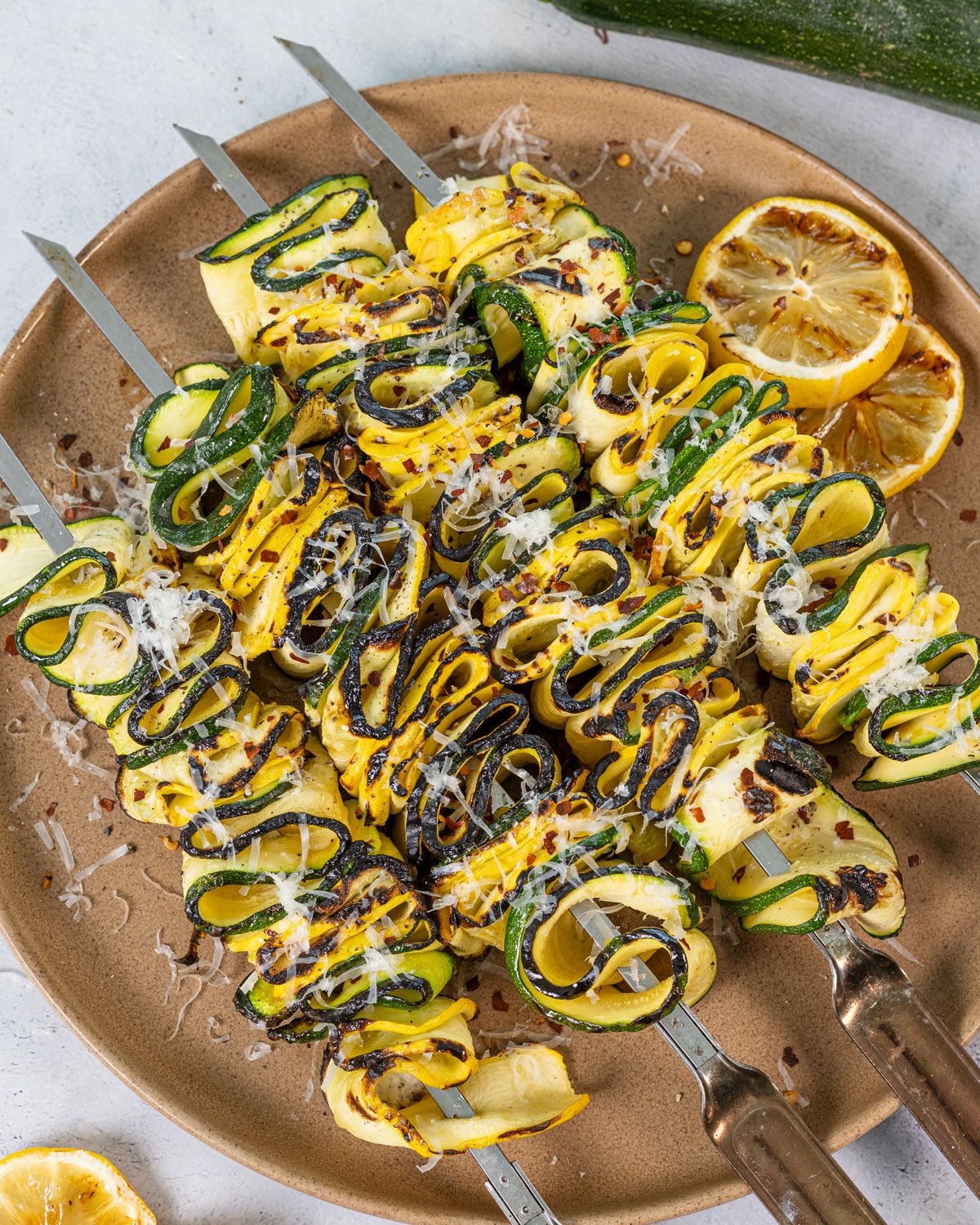 Zucchini and squash skewers on a platter after being grille with charred lemon slices on the side. 