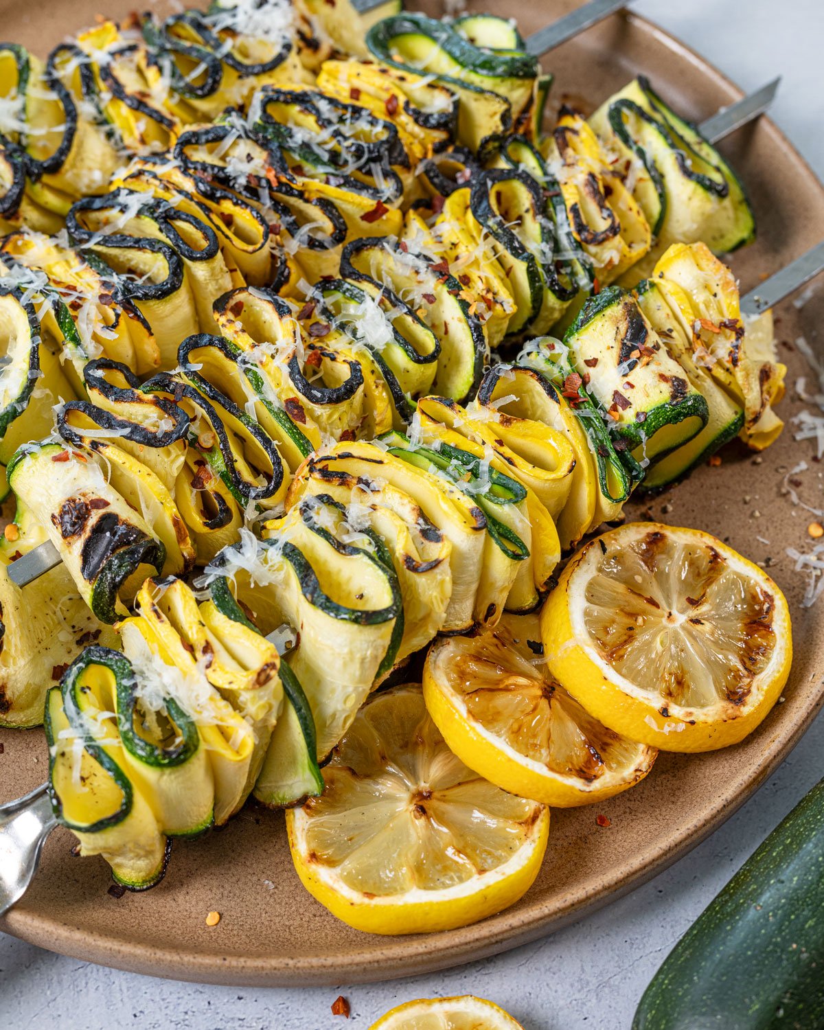Grilled zucchini squash skewers on a platter with charred lemons.