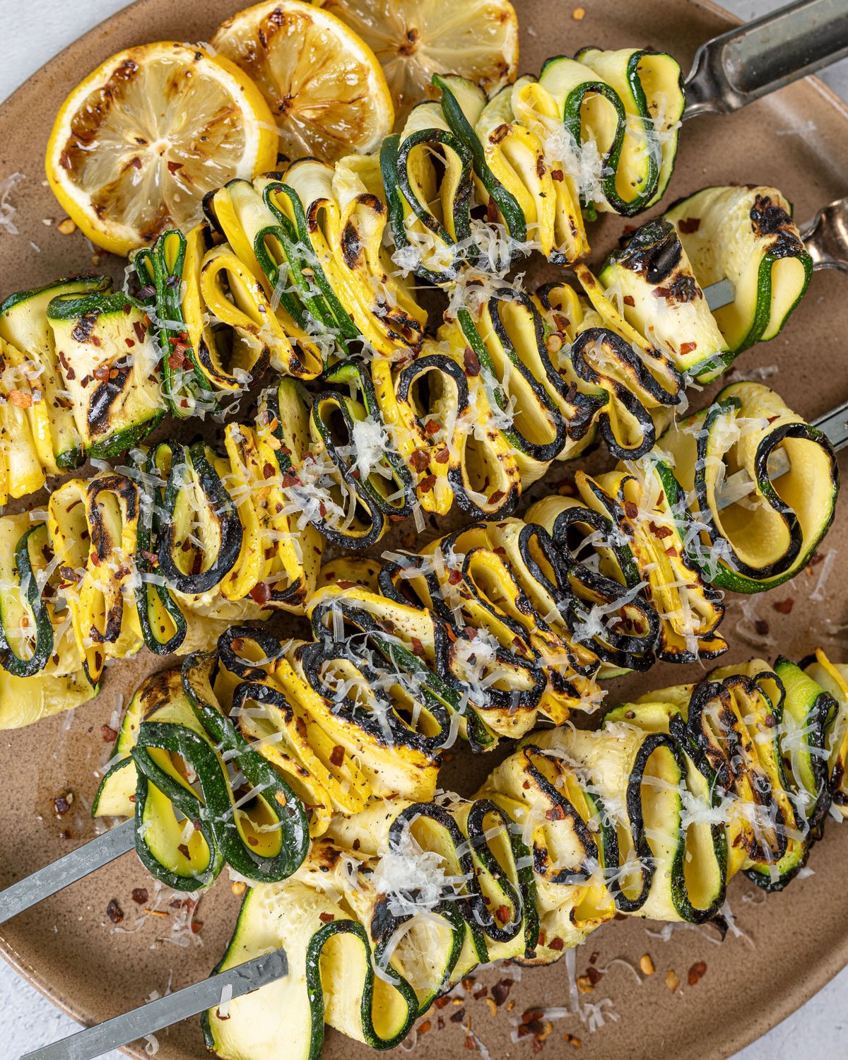 Grilled zucchini squash skewers on a platter topped with parmesan and red pepper flakes.