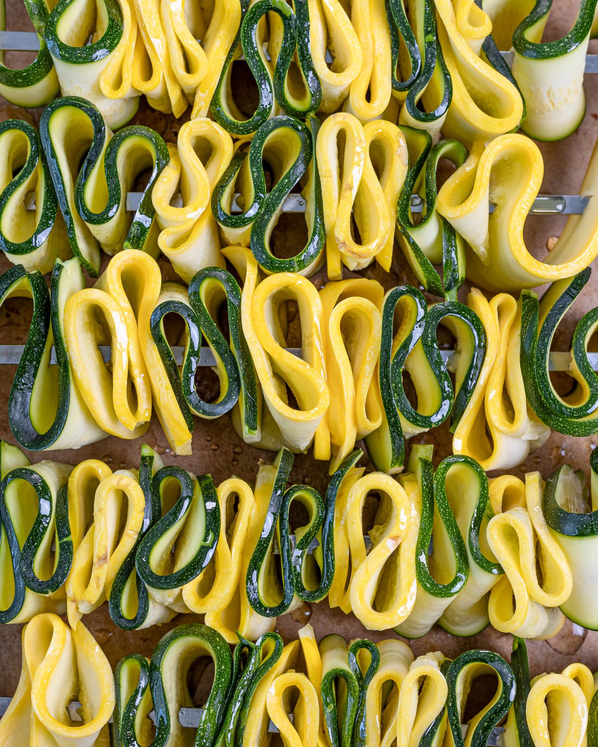 Fresh zucchini and squash ribbons weaved onto metal skewers before being grilled.