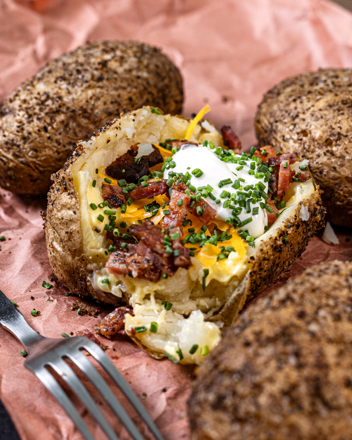 Smoked baked potatoes are topped with smoked bacon and laying on a paper with a fork