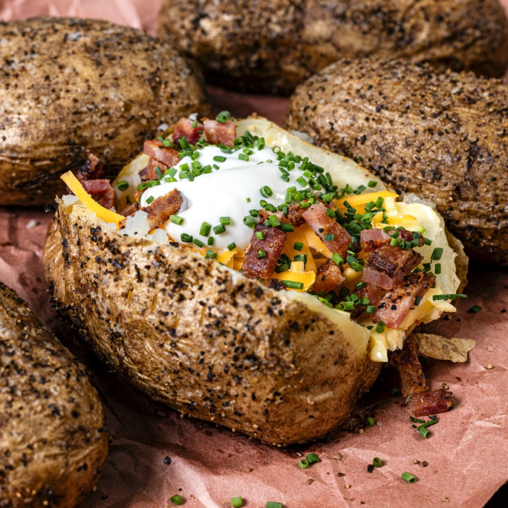 Smoked baked potatoes are loaded with sour cream, smoked bacon, and more toppings