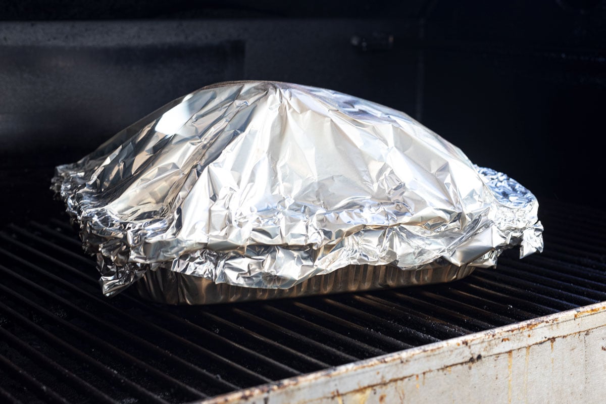 Ham is wrapped in a foil pan and placed in the smoker to braise
